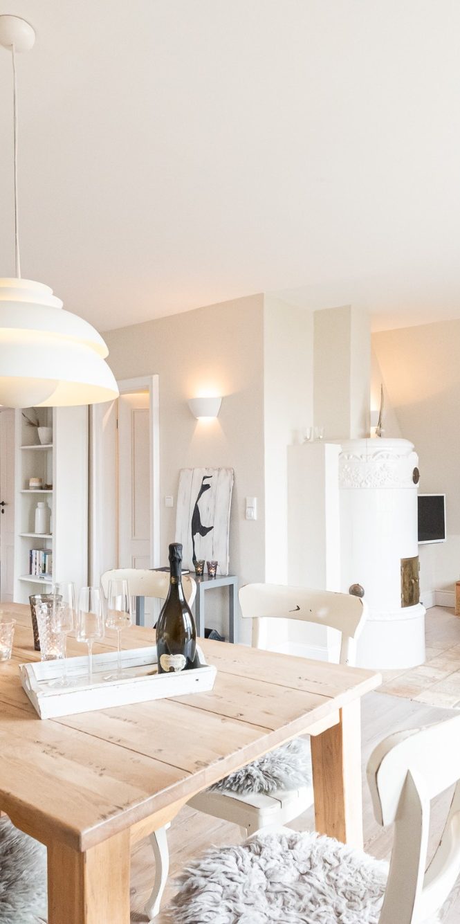 Im Wohnzimmer vom Sommerhaus Malmö in Wenningstedt steht ein Esstisch im Vordergrund und im Hintergrund ist ein schwedischer Kachelofen.